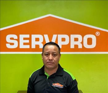 Brown haired male standing in front of a SERVPRO green background with a SERVPRO logo on the wall. 