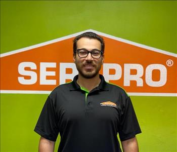 Brown haired male with glasses standing in front of a SERVPRO green background with a SERVPRO logo on the wall. 