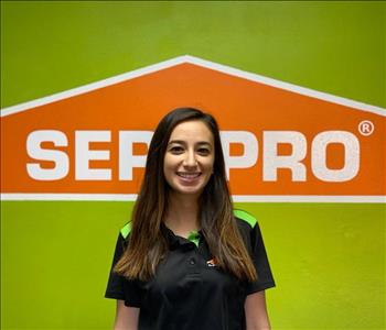 Brown haired female standing in front of a SERVPRO green background with a SERVPRO logo on the wall. 